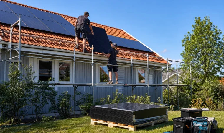 Installatörer lyfter solpaneler upp på ett tegeltak från en byggställning